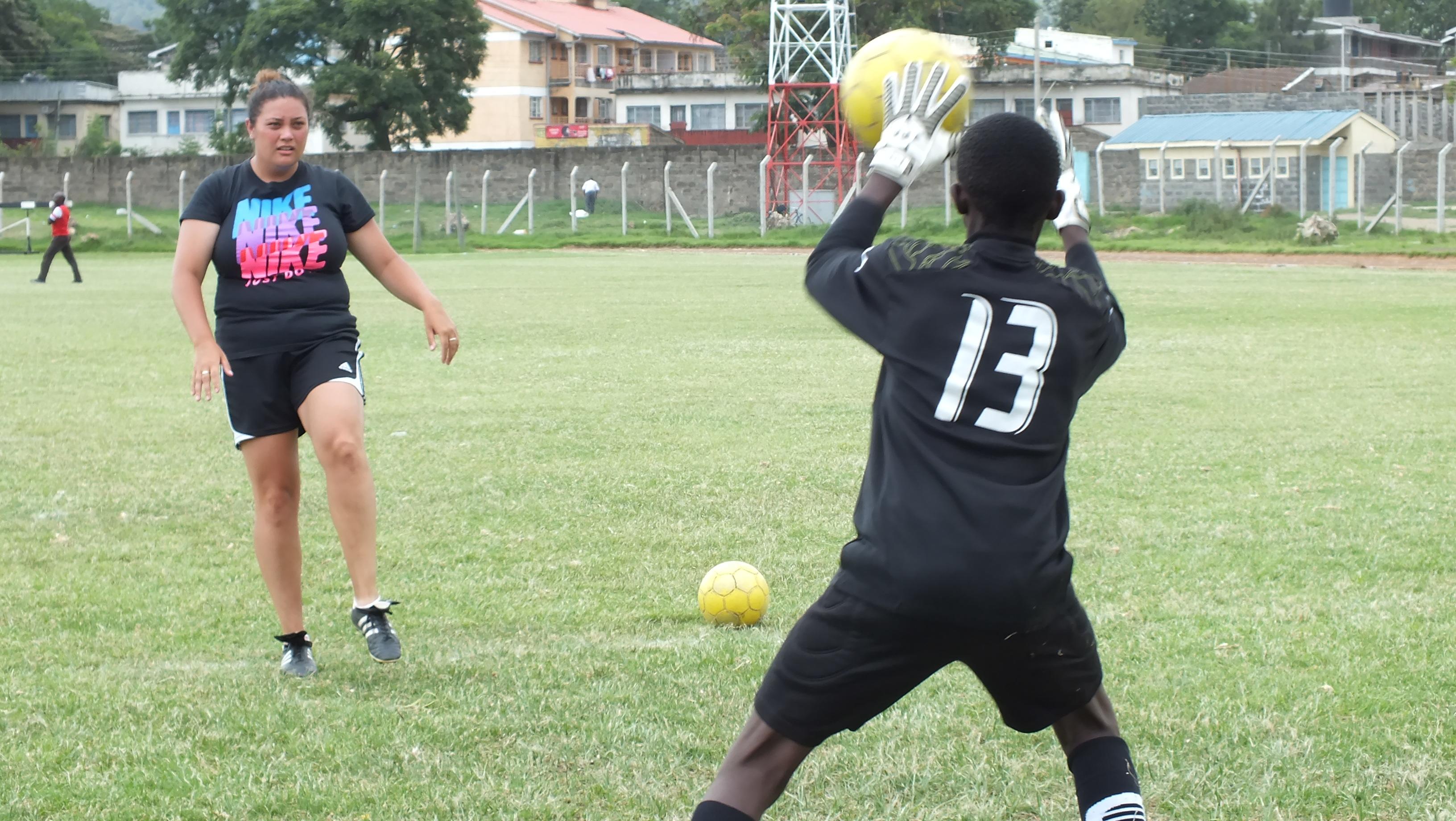 A Projects Abroad volunteer teaching sports in Kenya helps a player practise defending the goal A football player practises defending the goal during volunteer sports coaching in Kenya